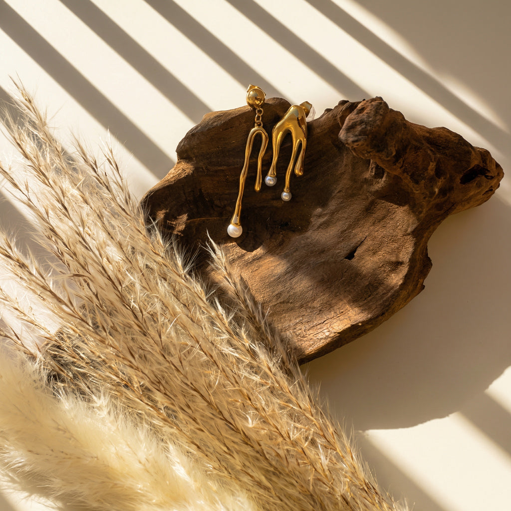 Nacre gold earrings pair laid flat, highlighting the molten form and pearl tips